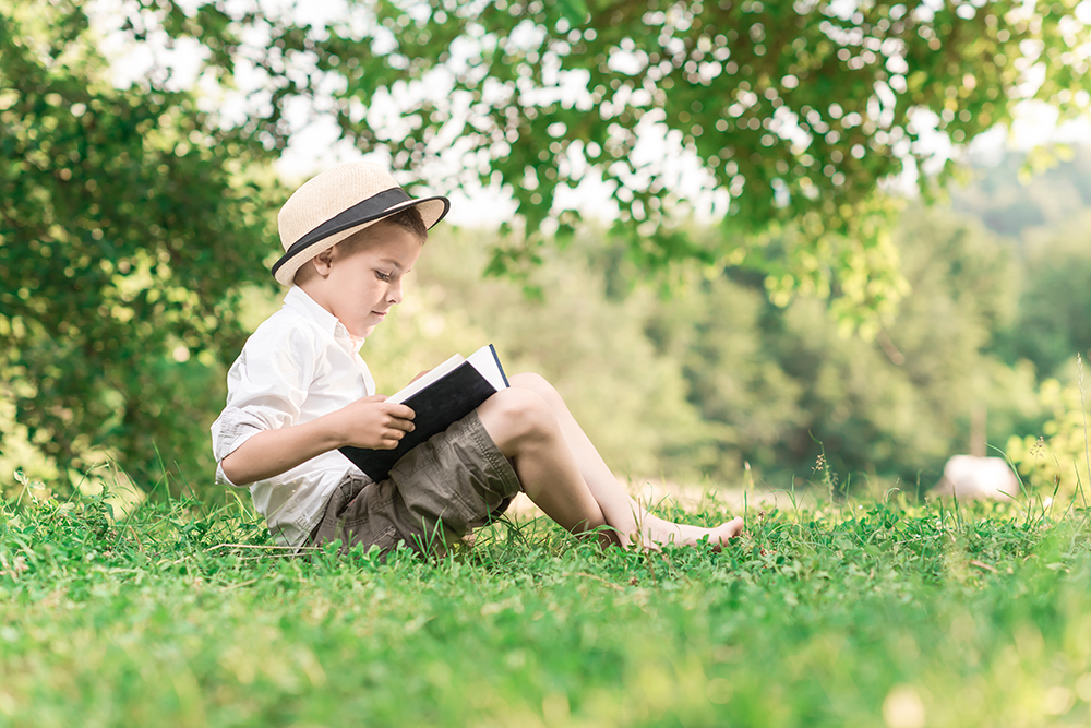 Boy reading a book outside as part of his teacher-led homeschooling online